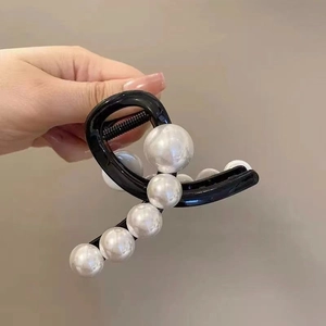Detailed view of hand holding a black shark clip hair claw with large white pearls