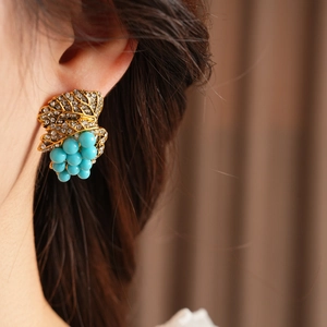 Macro detail of vintage grape leaf earrings in antique gold with blue rhinestone beads