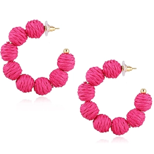 Detail of pink raffia beaded hoop earrings with gold metal studs on a white background