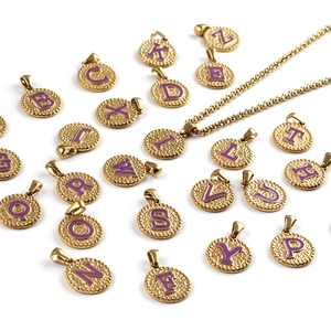 Detailed view of golden stainless steel pendants with purple enamel letters on white background