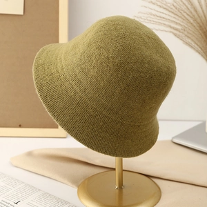 Olive green knitted bucket hat for women on a gold stand with autumn decorations