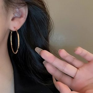 Close-up of a large gold metallic hoop earring worn by a model with a minimalist design