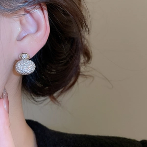 Macro close-up of zircon paved silver ball stud earrings worn by an elegant model