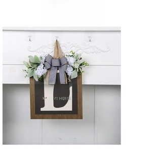 Detail of wooden door wreath with white letter L, artificial flowers and burlap bow decoration