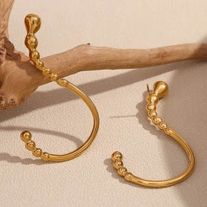 Macro detail of gold-plated stainless steel curved earring on a natural wooden branch