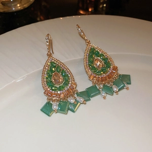 Close-up of vintage gold teardrop earrings with green gemstones and pearls on ceramic