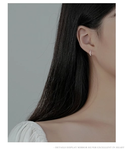Macro detail of silver diamond-encrusted rhombic earring on ear showing the mirror finish