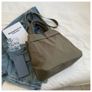 Flat lay detail of an army green nylon tote bag with wide straps on a white linen background