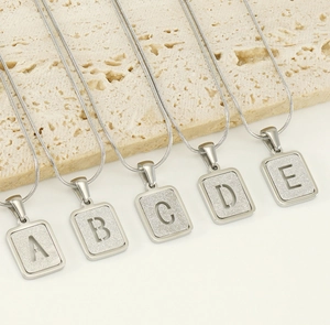 Détail macro de pendentifs alphabet A-E argentés avec texture mate et chaîne serpent fine
