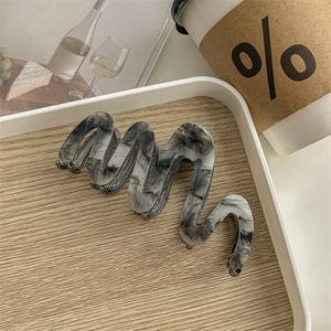 Macro detail of wave-shaped acetate hair claw clip with marble texture on wooden tray
