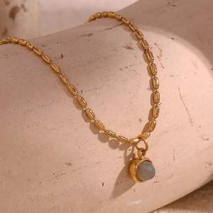 Macro shot of 18K gold beaded chain necklace with a round grey natural stone pendant