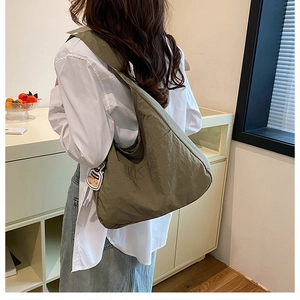 Olive green nylon tote bag shown on shoulder in a stylish modern interior setting