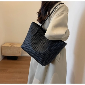 Detail shot of black woven faux leather tote bag carried on a woman's shoulder
