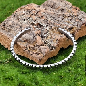Close-up of a punk-style silver skull cuff bracelet on natural mossy tree bark