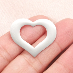 Polished silver hollow heart pendant accessory displayed on finger with fabric background