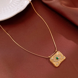 Gros plan du collier en acier doré avec pendentif carré œil protecteur et gemme verte