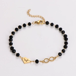 Macro shot of gold chain bracelet with black faceted beads and heart infinity charms