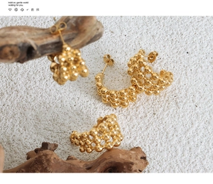 Macro detail of gold-plated C-shaped earrings with bead texture on stone background