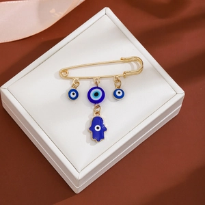 Detail shot of golden safety pin brooch featuring blue evil eye and Hamsa hand charms