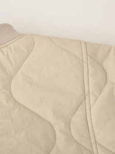 Detailed macro view of beige quilted jacket with wave patterns and ribbed collar texture