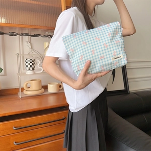 Floral makeup bag with blue plaid and pink bow patterns held by a model in a home setting