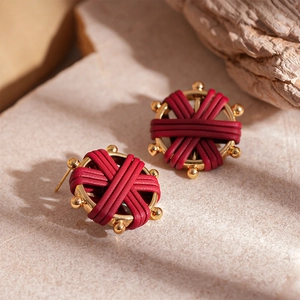 Detail of red woven leather layered on golden metal hoop earrings with vintage texture