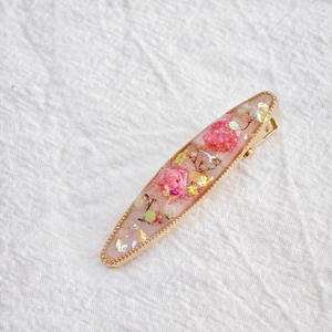 Detailed close-up of a golden clip with real pink dried flowers and gold glitter flakes
