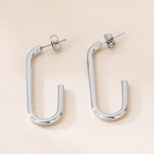 Détail de boucles d'oreilles géométriques argentées en U sur tissu de soie beige