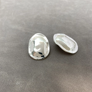 Macro shot of silver irregular pebble earrings with a polished metallic finish on grey