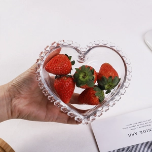 Close-up of heart-shaped glass plate holding fresh strawberries on a minimalist desk