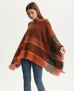 Close-up of herringbone pattern and fringe details on an orange knit hooded poncho