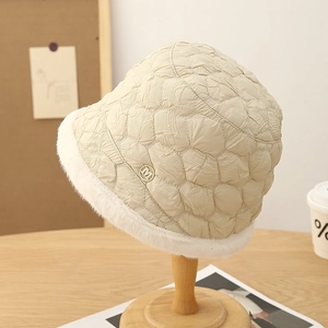 Warm beige quilted bucket hat with faux fur trim and gold M logo on a wooden stand