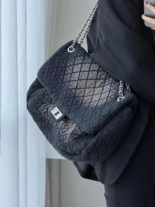 Close-up of black quilted denim shoulder bag with metal chain strap and twist-lock