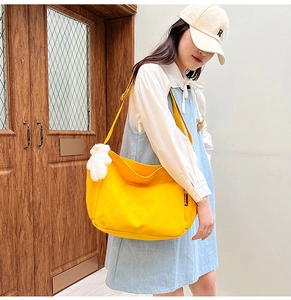 Detailed shot of yellow canvas crossbody bag with a white plush bear charm accessory