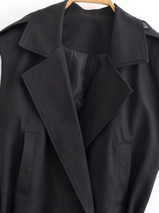 Détail du gilet noir à col revers avec pattes d'épaule et texture de tissu tissé