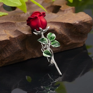Detailed view of 3D matte red rose brooch with green enamel leaves on a wooden prop