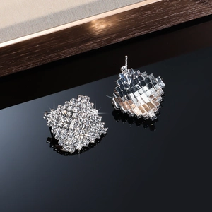 Macro shot of silver square stud earrings with sparkling pave-set rhinestones on reflective glass