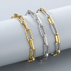 Detail of paperclip chain bracelets in gold, silver, and two-tone finishes on grey display
