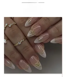 Detail of short almond press-on nails with white gradient and 3D metallic bow charms