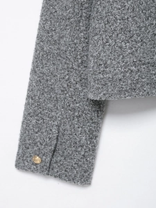 Detail shot of grey bouclé texture jacket featuring metallic gold buttons on the cuff