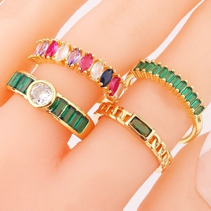 Detail view of four emerald cubic zirconia rings in gold plating worn on fingers