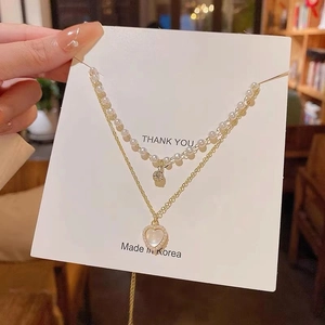 Detail of double-layer necklace with white pearls and a sparkling heart opal pendant