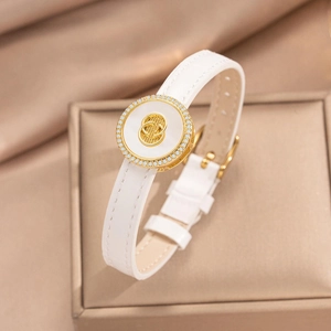 White leather bracelet with gold circular charm and inlaid crystals on elegant jewelry box