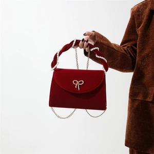 Detail of red velvet handbag featuring golden bow clasp and pearl-intertwined handle