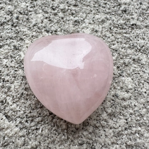 Detailed macro shot of a 3cm heart-shaped natural pink quartz crystal on a textured stone base