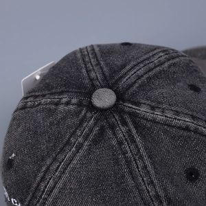 Close-up of distressed charcoal grey denim baseball cap with white embroidery and eyelets