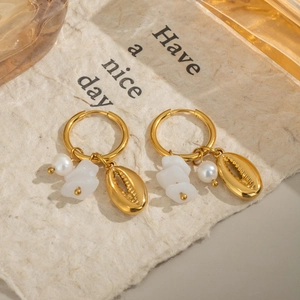 Créoles dorées avec pendentifs perles et coquillages sur fond texturé