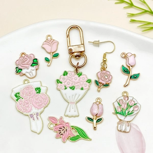 Pink enamel rose and tulip flower pendants in gold finish on a white ceramic plate