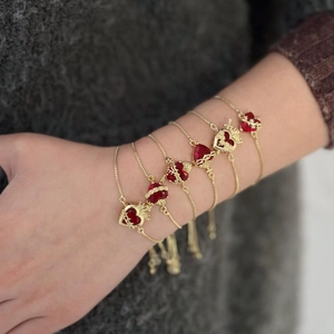 Primo piano di bracciali regolabili in oro con ciondoli a cuore rosso su un polso.