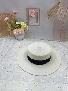 Detailed weave of flat top straw boater hat with black ribbon on floral tablecloth